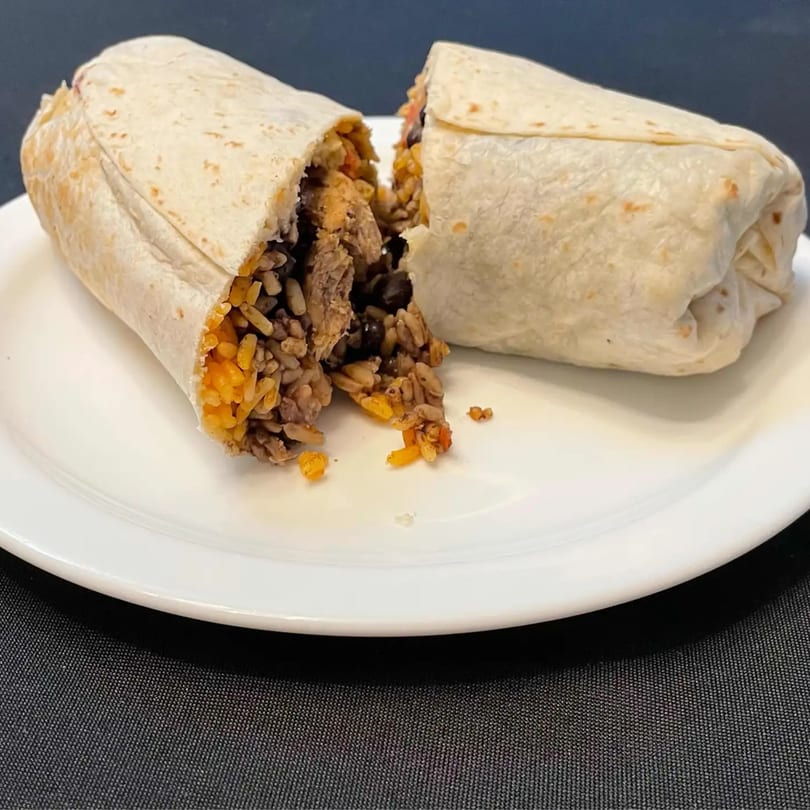 A large El Vaquero Mexican Taqueria burrito, cut in half, revealing rice, beans, and meat.