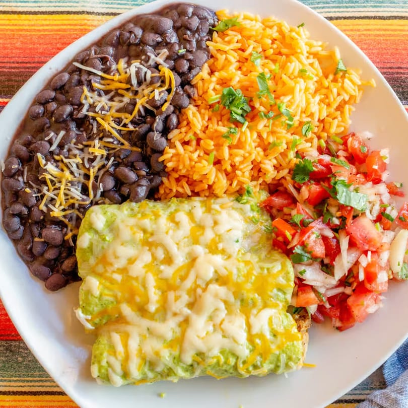 El Vaquero Mexican Taqueria's enchiladas with rice, black beans, and pico de gallo on a white plate.